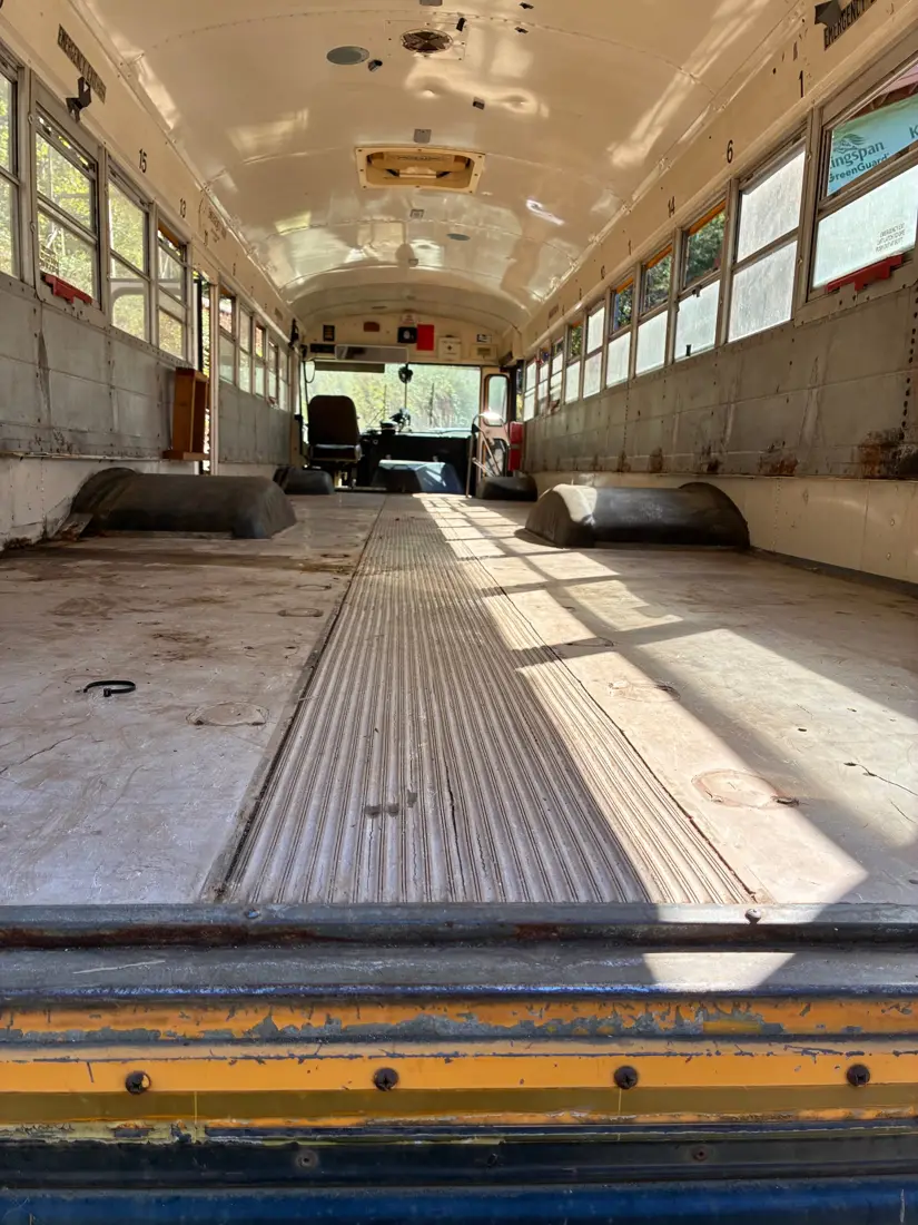 Inside the stripped bus looking toward the driver seat, with bare floor and open windows